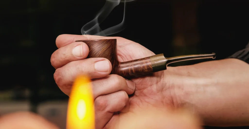 A hand holds a pipe with smoke coming out of the top.