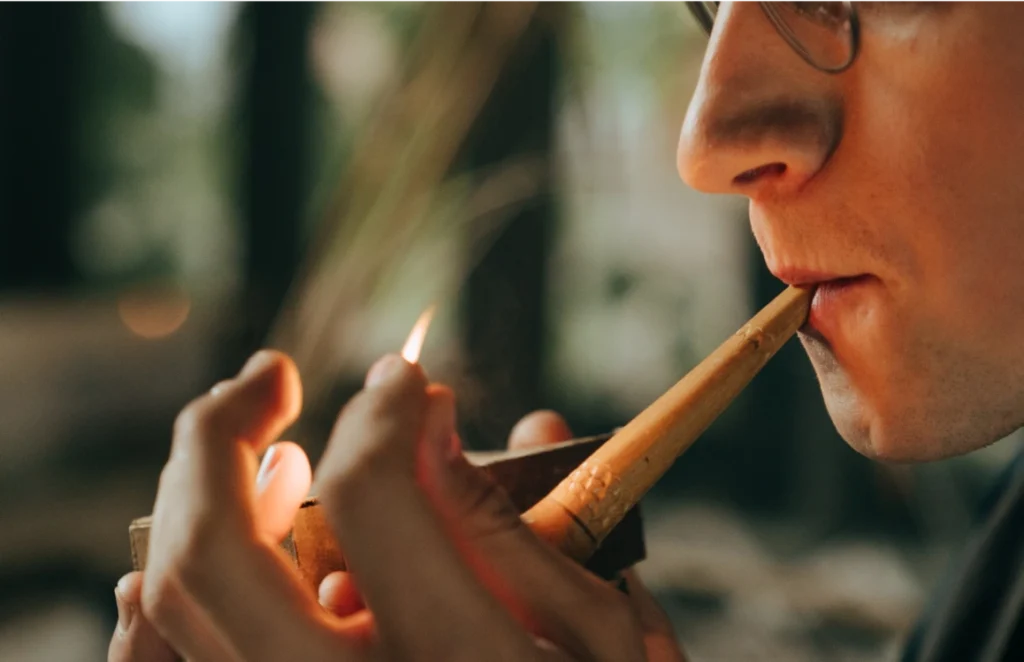 Close-up of a man lighting a handmade tobacco pipe with a match.